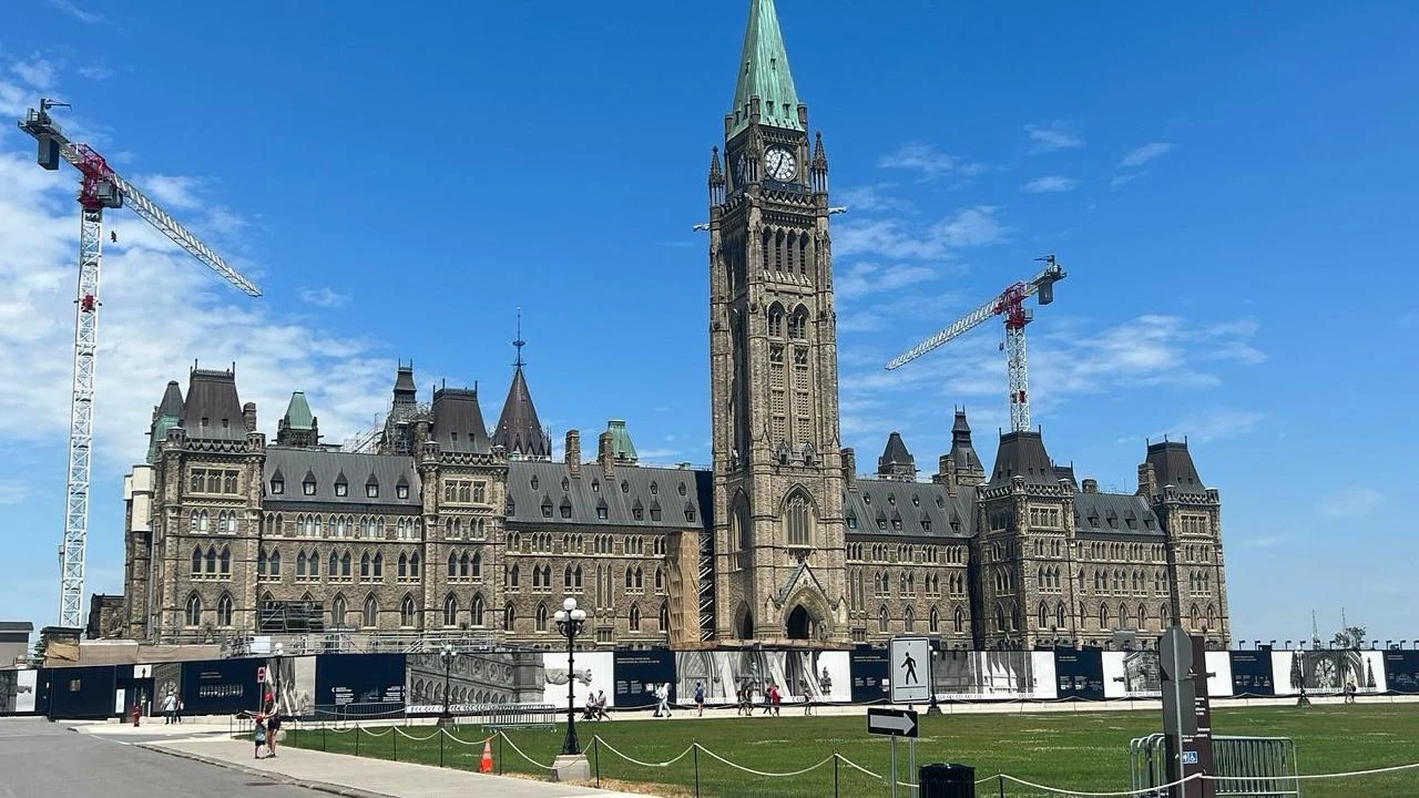 Parlamentsgebäude mit hohem Uhrturm und Baukränen unter blauem Himmel in Ottawa