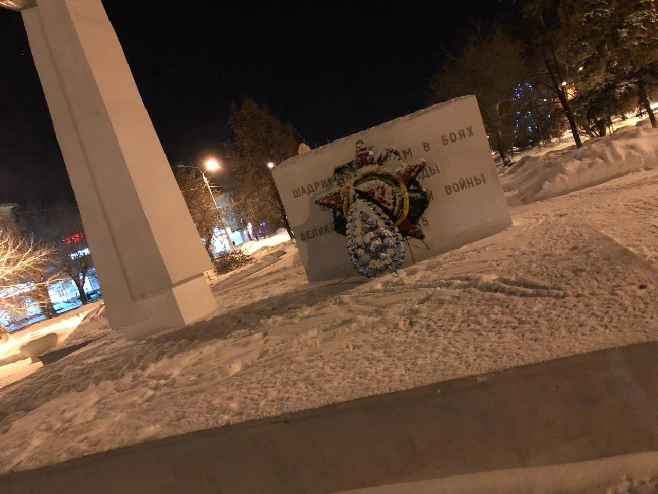 Verschneites Denkmal mit Kränzen und Obelisk bei Nacht in Shadrinsk
