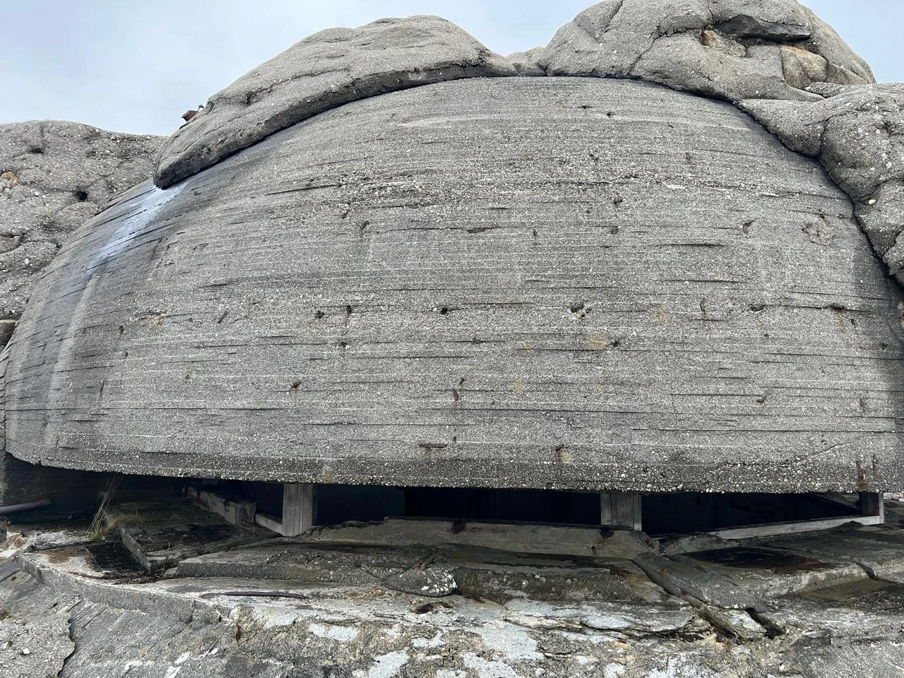 Massives Betonbauwerk mit schmaler horizontaler Öffnung zwischen grauen Felsen